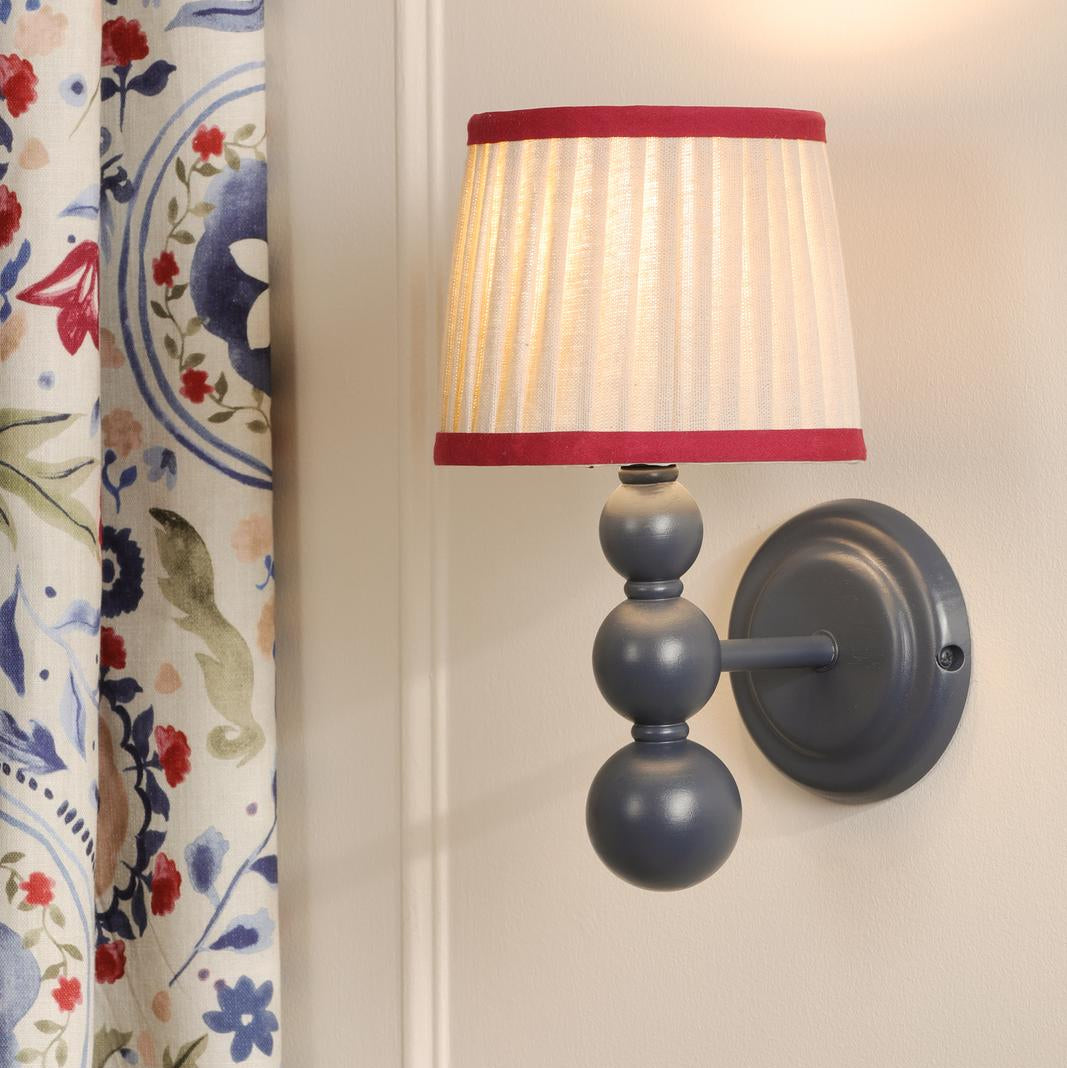 Wall sconce with a blue spherical stem and a pleated fabric shade with red trim