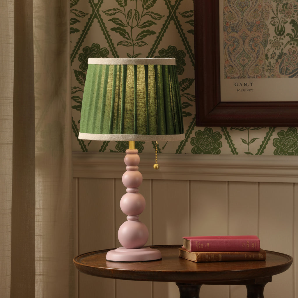 Table lamp with a pink stacked sphere base and a pleated green fabric shade on a wooden table