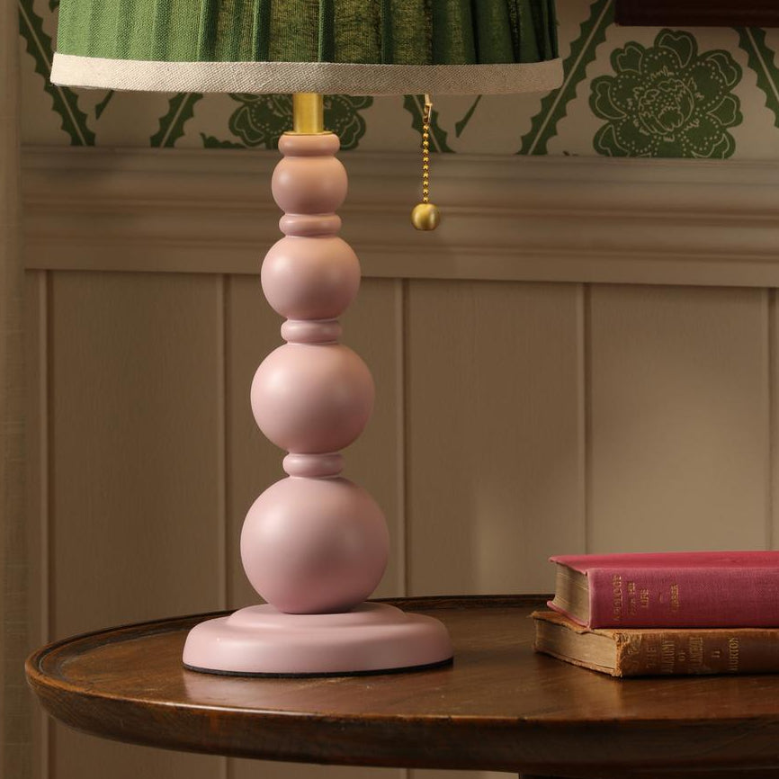 Joules Harewood table lamp in matt pink with a green pleated linen shade on a wooden table
