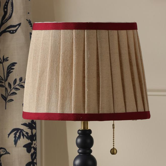 Beige pleated lampshade with red trim and brass pull chain