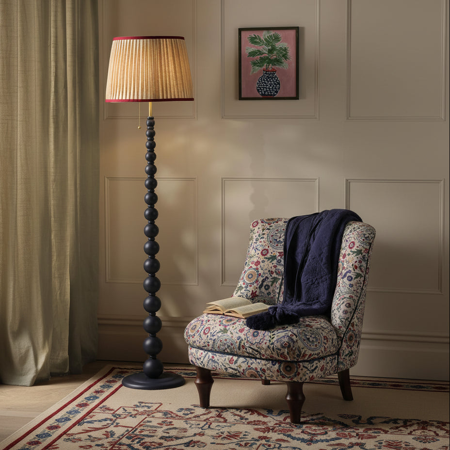 Black beaded floor lamp with pleated shade next to a floral patterned armchair
