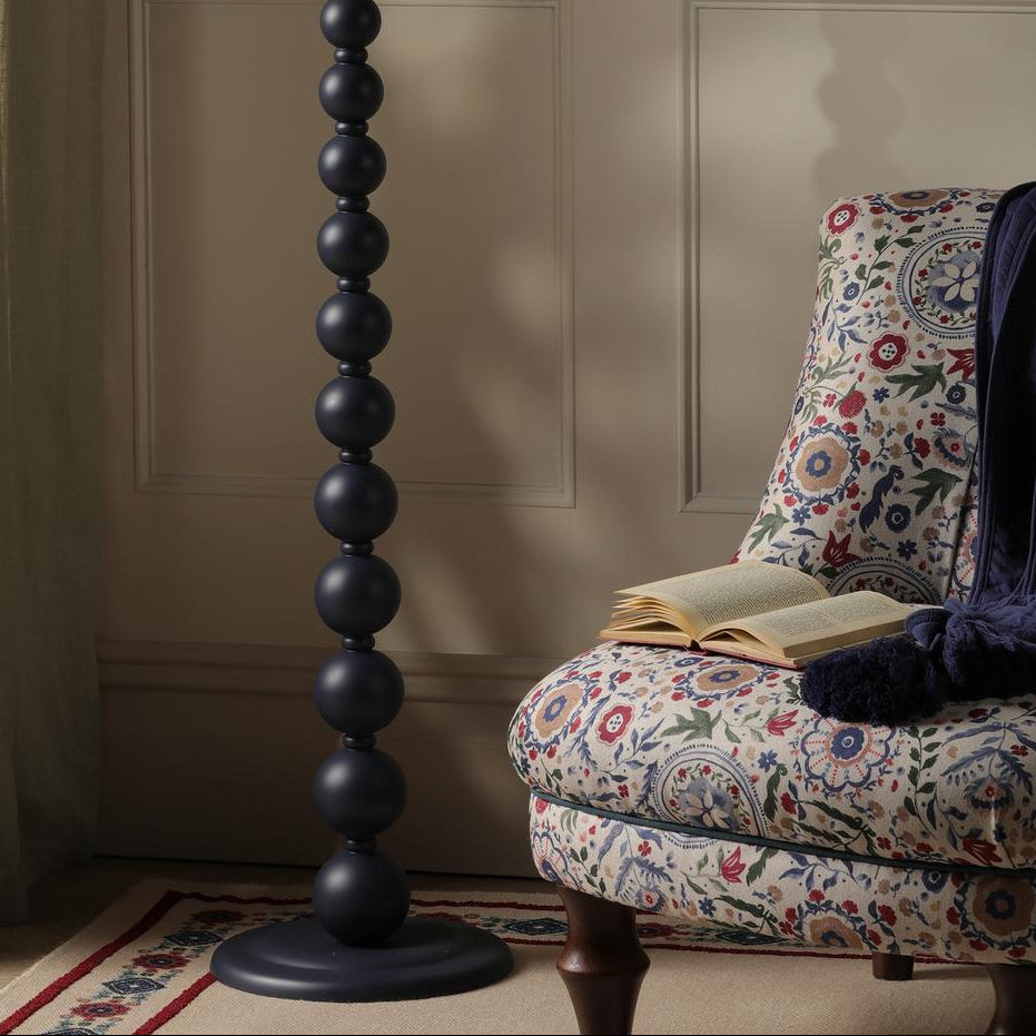 Joules Harewood floor lamp in matt blue with a stacked sphere base next to a patterned armchair