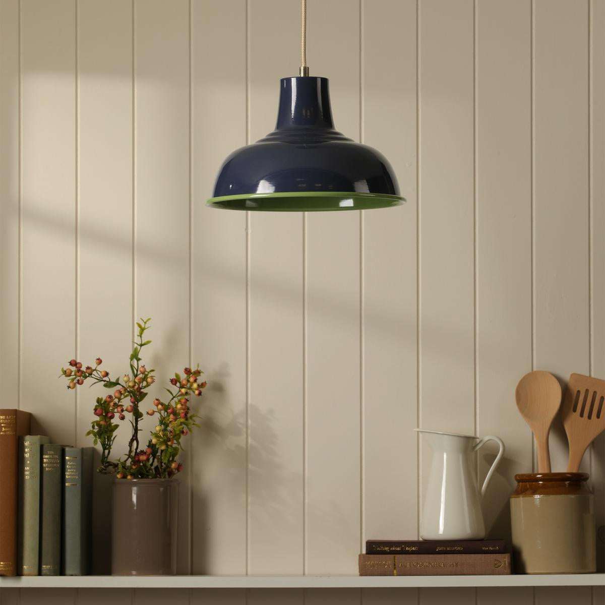 Navy blue and lime green metal pendant light hanging above a shelf with books and kitchen utensils