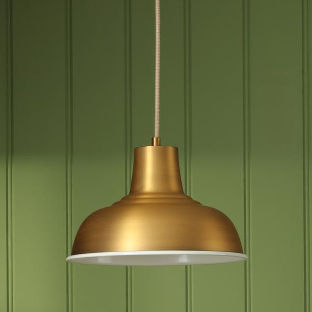 Brushed brass dome pendant light with white interior against a green paneled wall