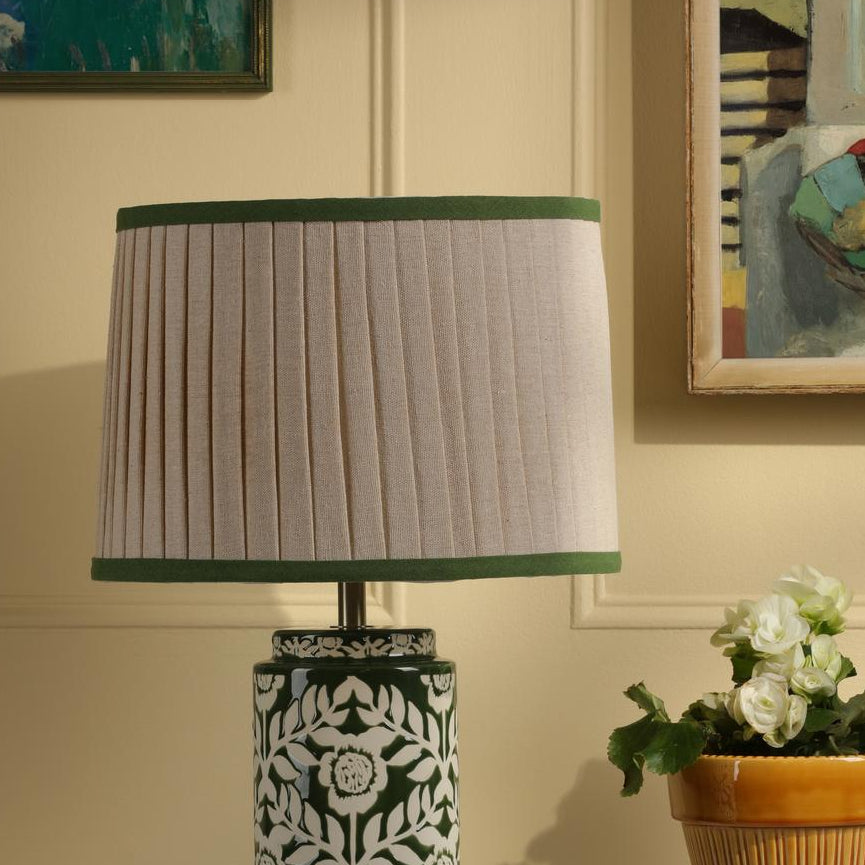 Pleated beige lampshade with green trim on a patterned green and white ceramic lamp base