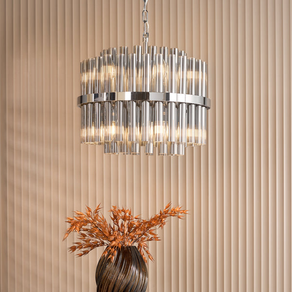 A chrome and glass chandelier hangs above a brown vase with dried orange foliage