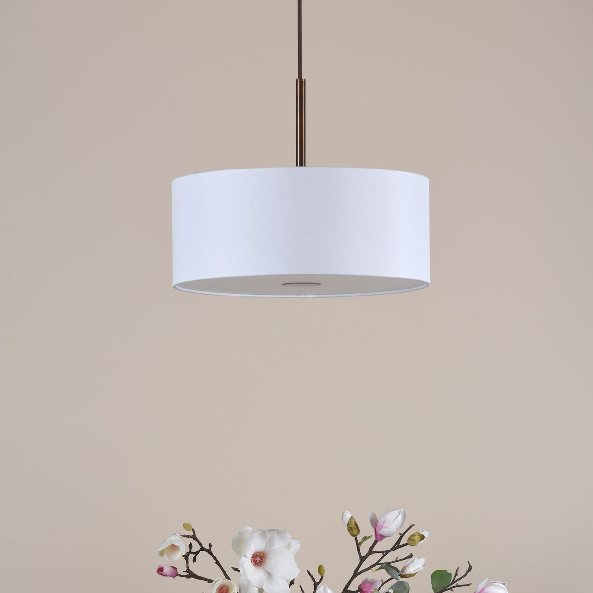 White drum pendant light with a bronze rod, above a bouquet of white and pink magnolia flowers