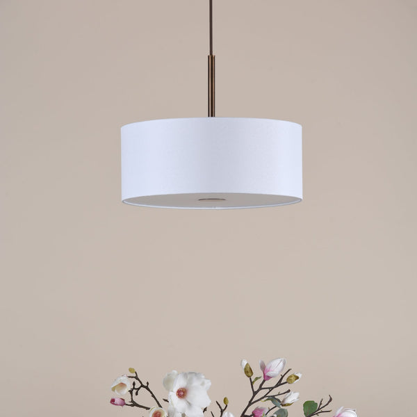 White drum pendant light with a bronze rod, above a bouquet of white and pink magnolia flowers