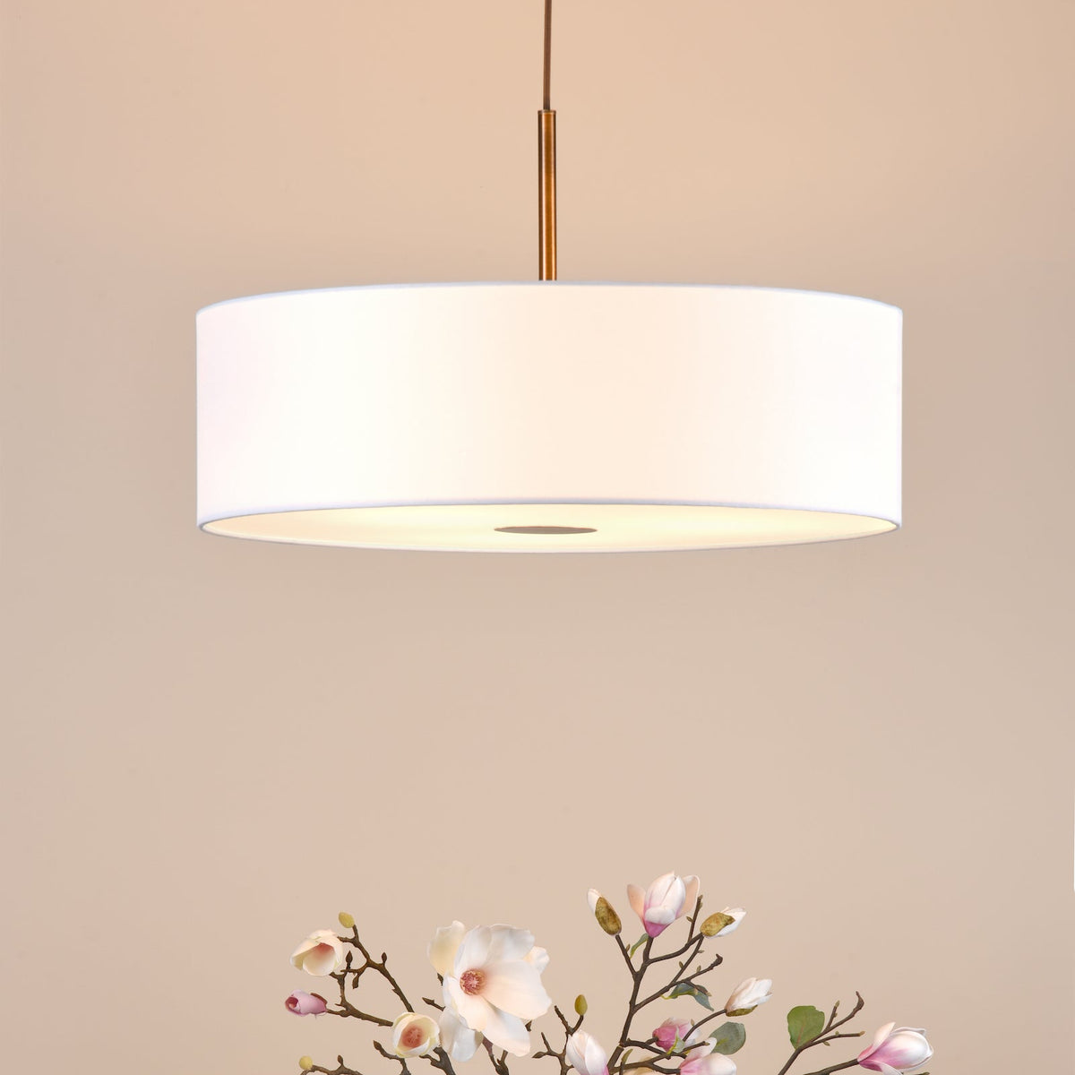 White drum pendant light with a gold rod and magnolia branches below