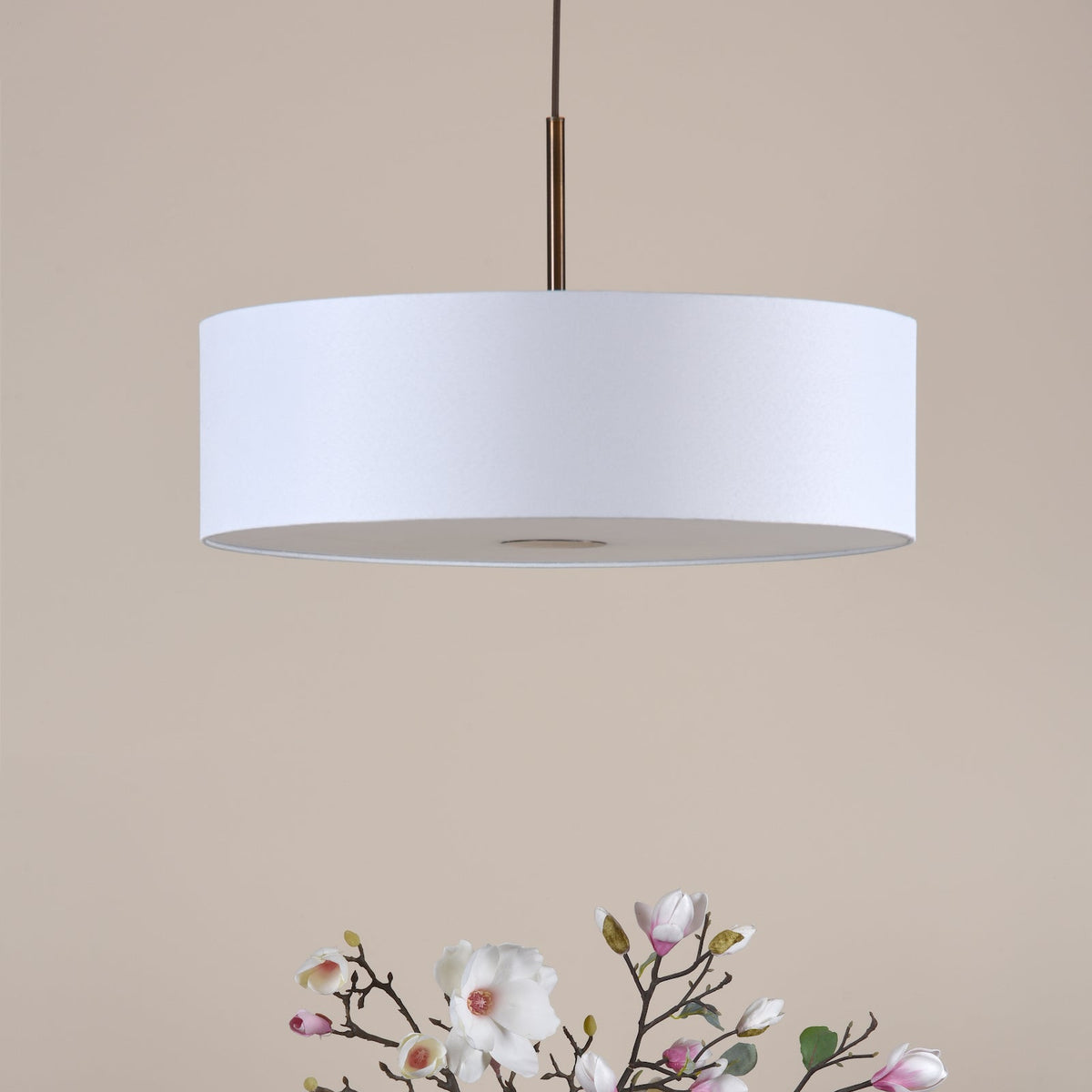 White drum pendant light with a bronze rod, above a bouquet of white and pink magnolia flowers