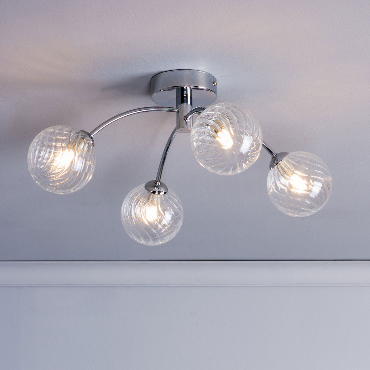 Chrome ceiling light with four clear, swirled glass globe shades, each illuminated.