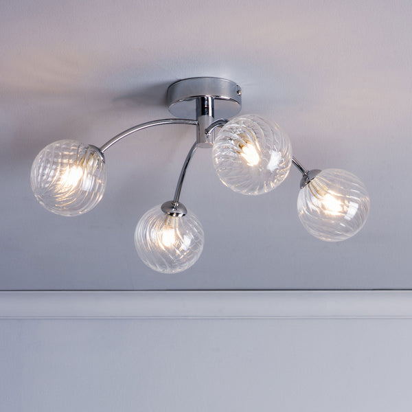 Chrome ceiling light with four clear, swirled glass globe shades, each illuminated.