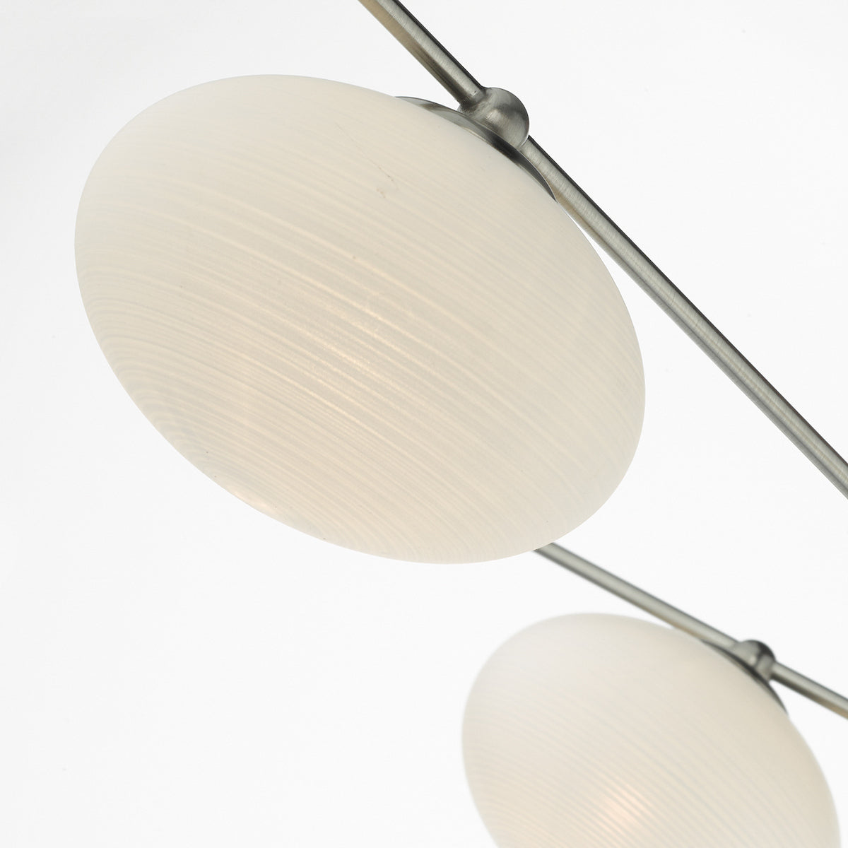 Close-up of two oval, white glass light shades with subtle horizontal lines, attached to a metal rod.