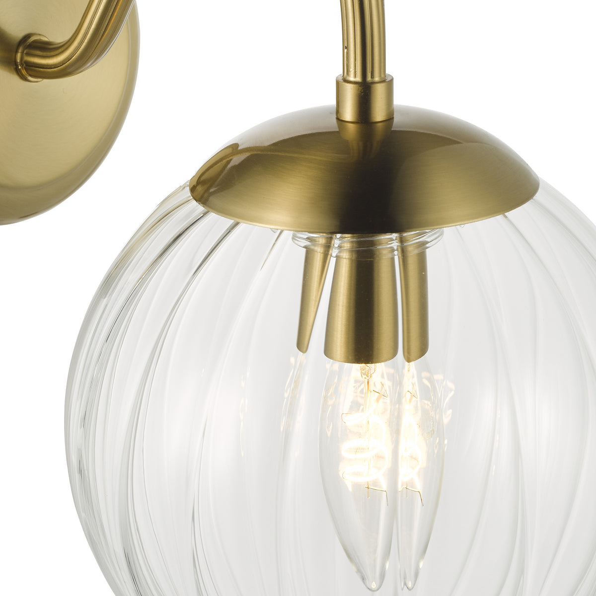 Close up of a brass wall sconce with a clear ribbed glass shade and an exposed filament bulb