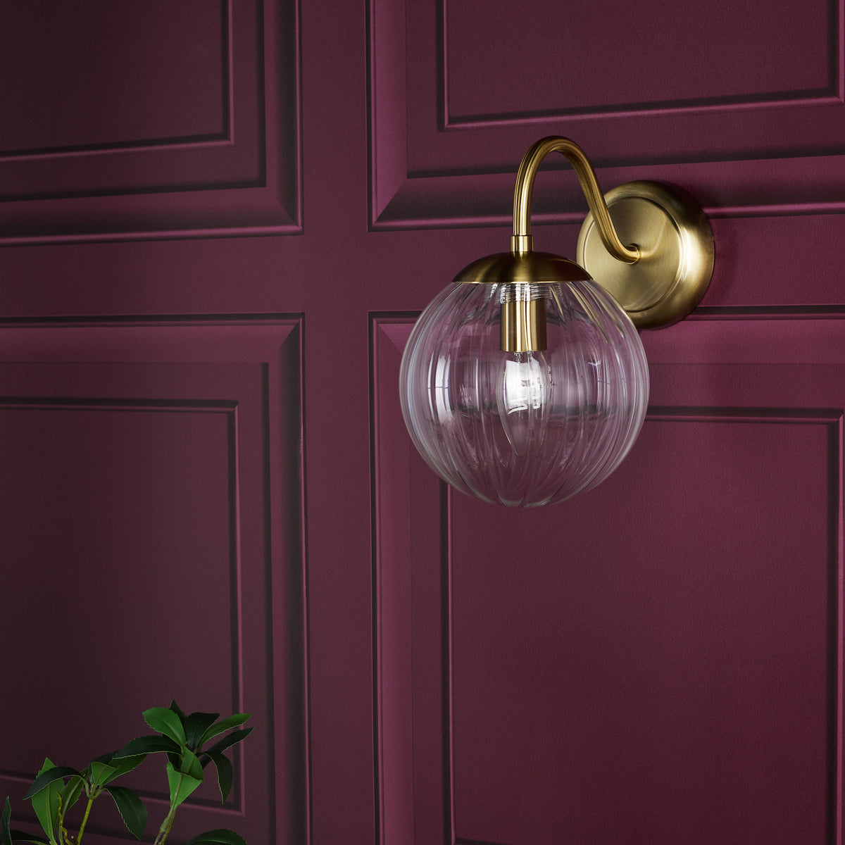 Brass wall sconce with a clear ribbed glass globe shade on a deep red paneled wall