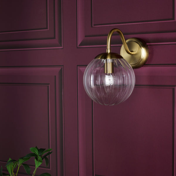 Brass wall sconce with a clear ribbed glass globe shade on a deep red paneled wall