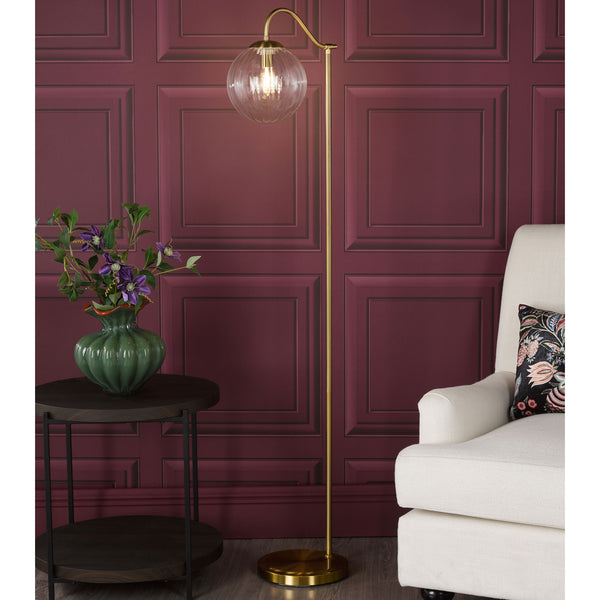 Gold floor lamp with a clear glass globe shade next to a cream armchair and a dark wood side table