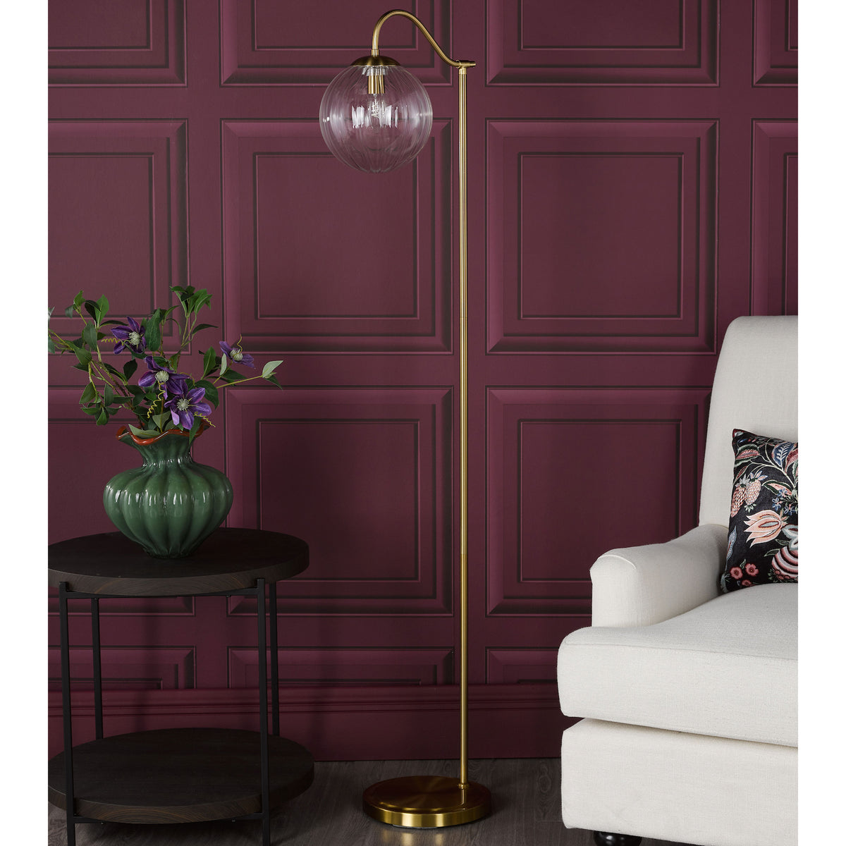 Brass floor lamp with a clear fluted glass shade next to a white armchair and a dark wood side table