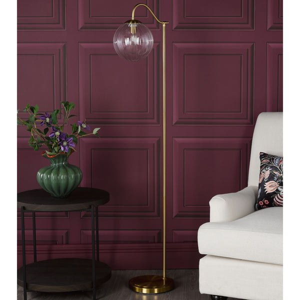 Brass floor lamp with a clear fluted glass shade next to a white armchair and a dark wood side table