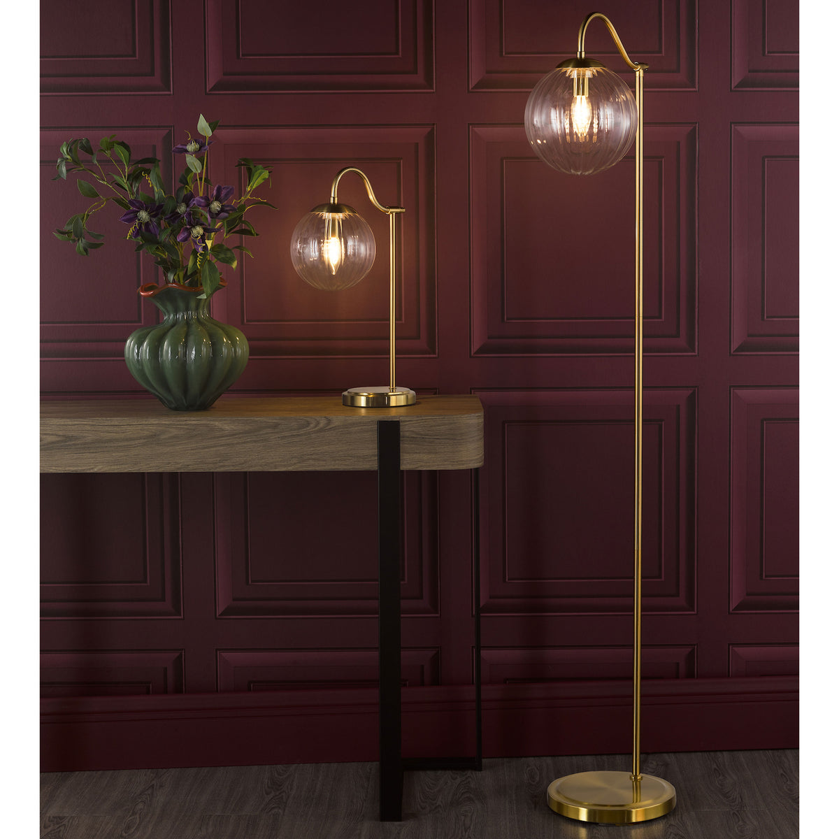 Two gold lamps with clear glass shades, one on a wooden console table with a green vase, the other a floor lamp