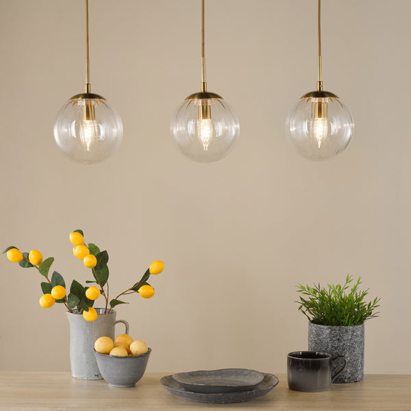 Three clear glass pendant lights with brass accents hang above a wooden table with decorative items