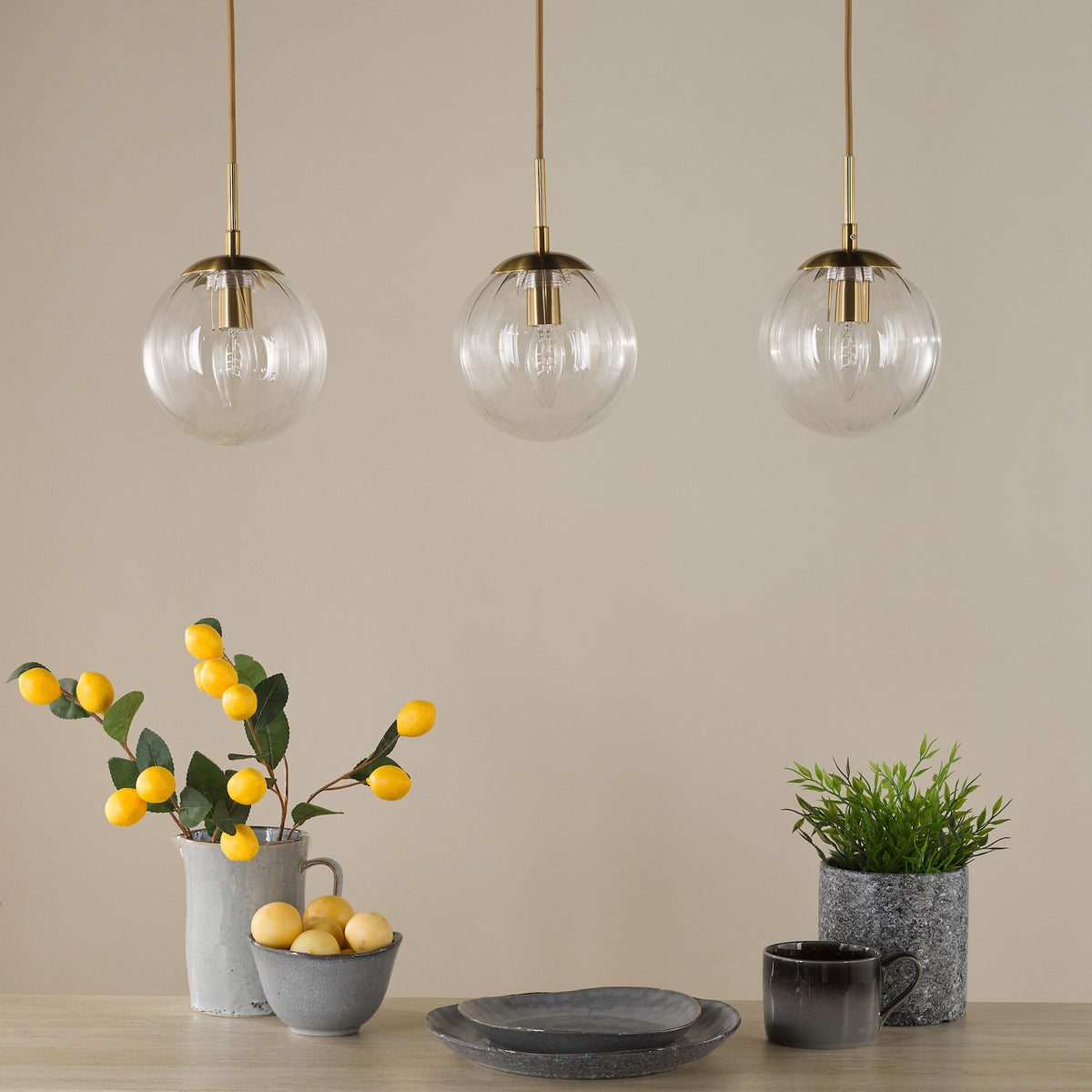 Three glass pendant lights above a table with a pitcher of lemons, a bowl of lemons, plates, and a plant