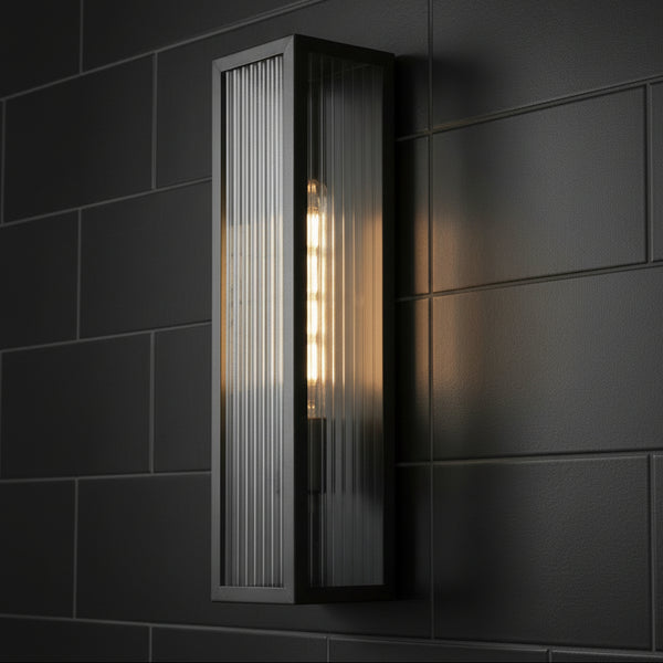 Rectangular wall sconce with ribbed glass and exposed bulb on a dark tiled wall