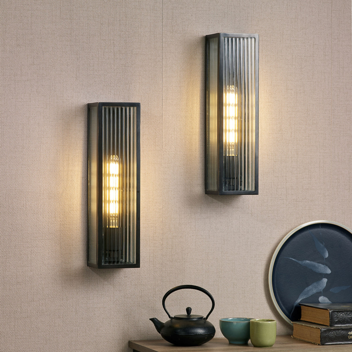 Two rectangular wall sconces with ribbed glass and black frames illuminate a textured beige wall