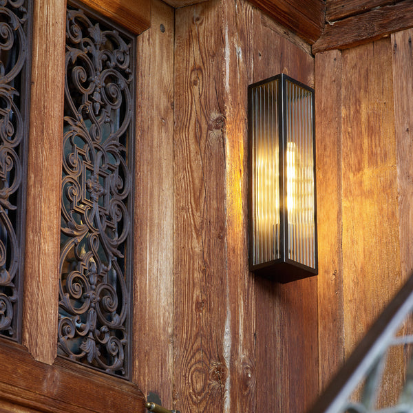 A close-up of a wooden wall with a decorative metal grate and a lit rectangular wall sconce