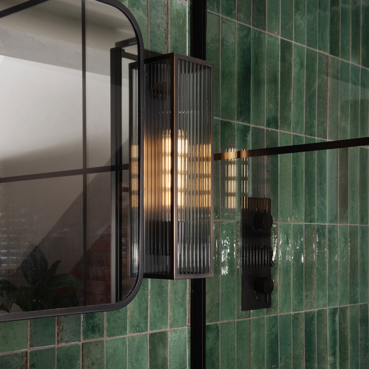 A close up of a bathroom with green tiles, a mirror, and a light fixture
