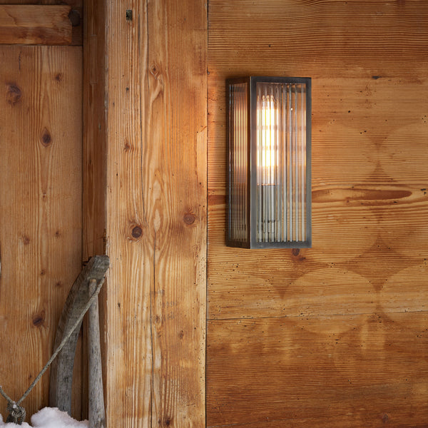 Rectangular outdoor wall light with ribbed glass and exposed bulbs on a wooden wall