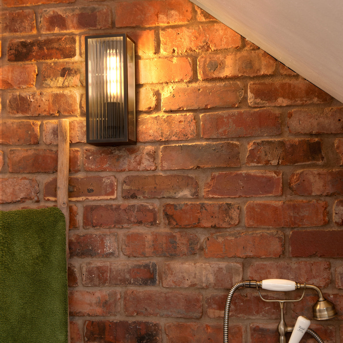 Black wall light with ribbed glass on a brick wall, with a green towel and shower head visible