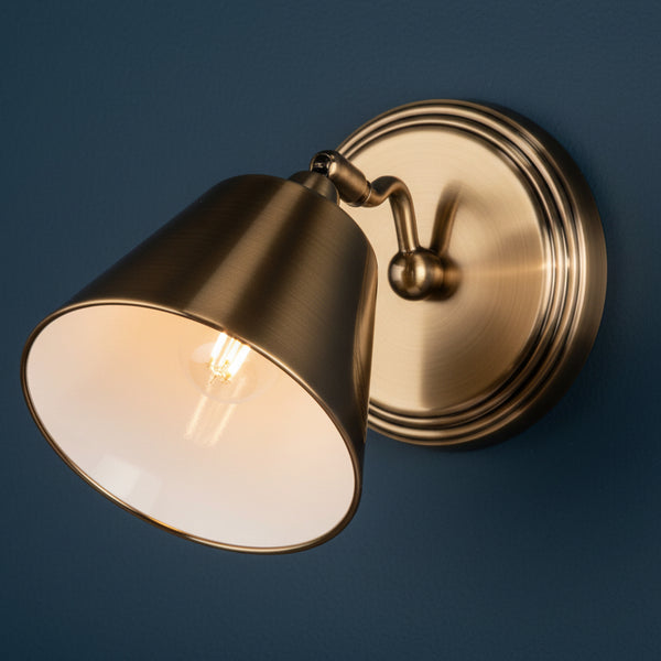 Brass wall light with a conical shade and exposed bulb on a dark blue wall