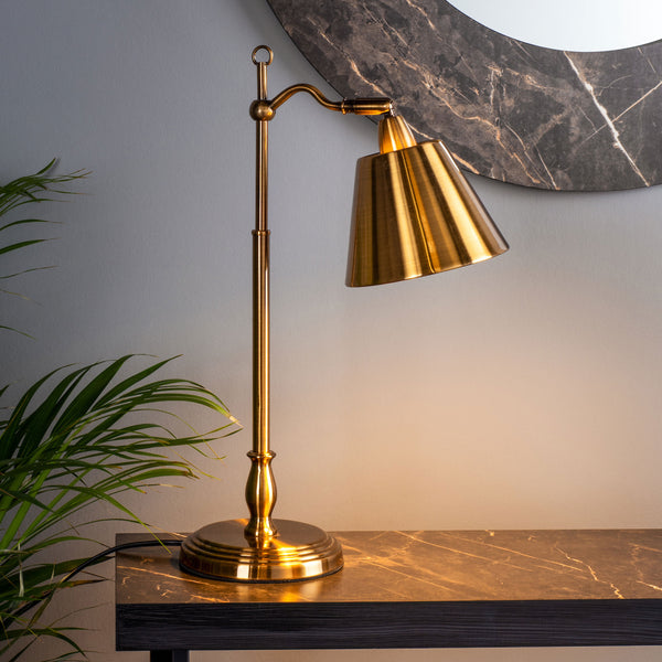 Brass table lamp with a conical shade and adjustable arm, on a dark marble-patterned surface