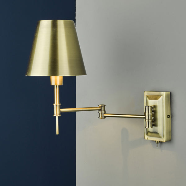 Brass wall lamp with a conical shade and an adjustable arm, mounted on a grey wall next to a dark blue wall