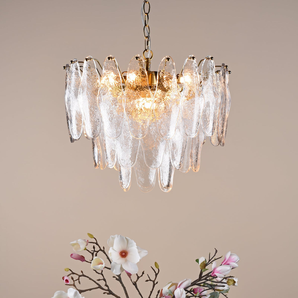 Chandelier with textured glass panels and a gold chain, above a branch with white and pink flowers