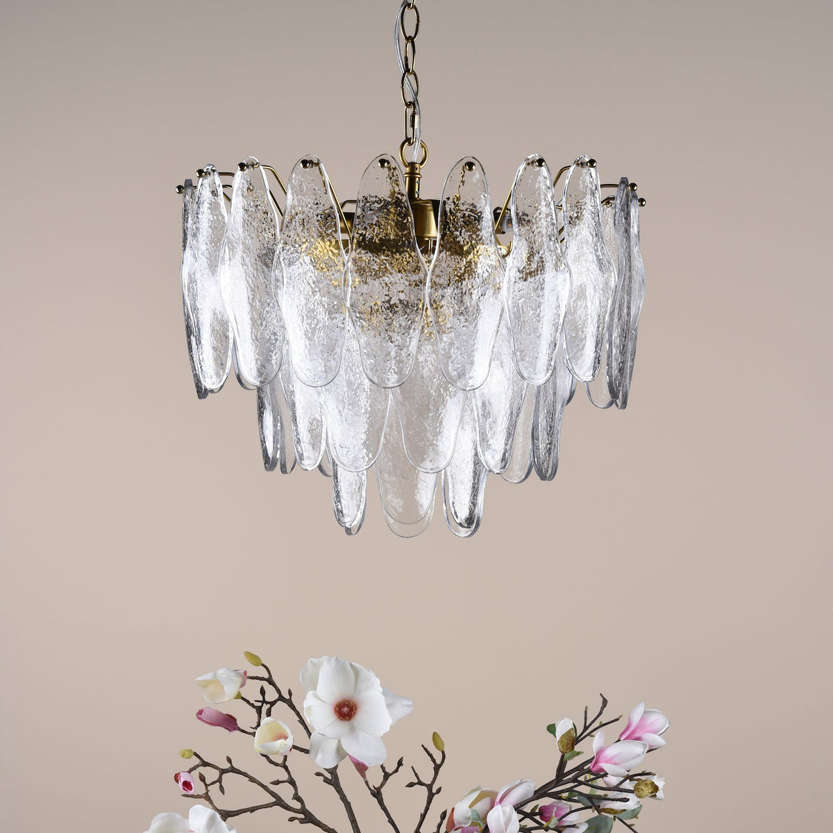 Chandelier with textured glass panels and a gold-flecked interior, above a branch with white and pink flowers