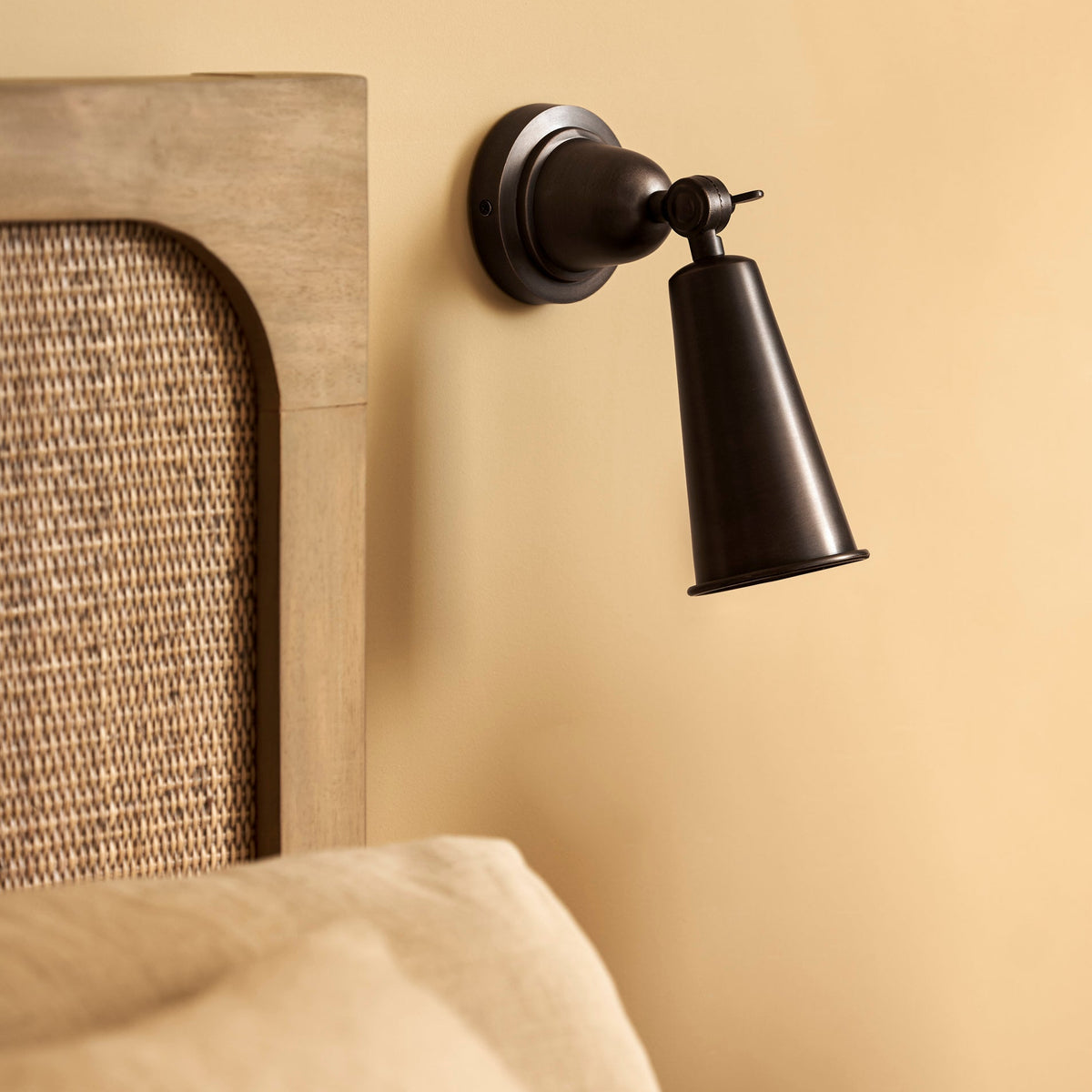 Longborough wall spotlight in antique bronze mounted on a wall next to a bed