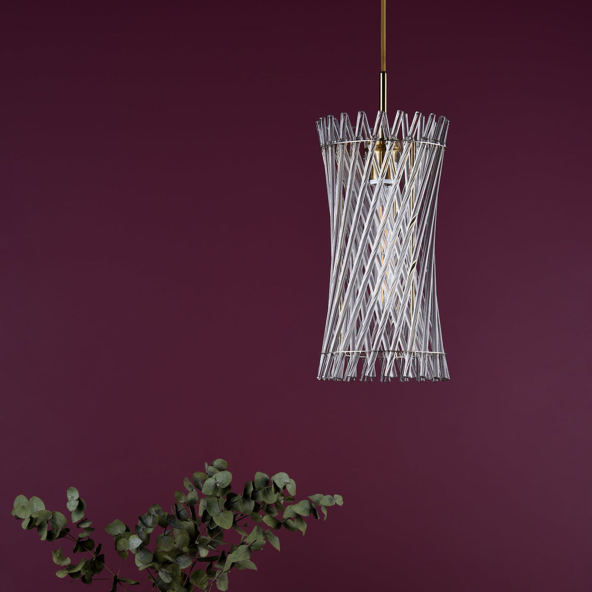 Glass tube chandelier against a plum wall with eucalyptus leaves in the foreground