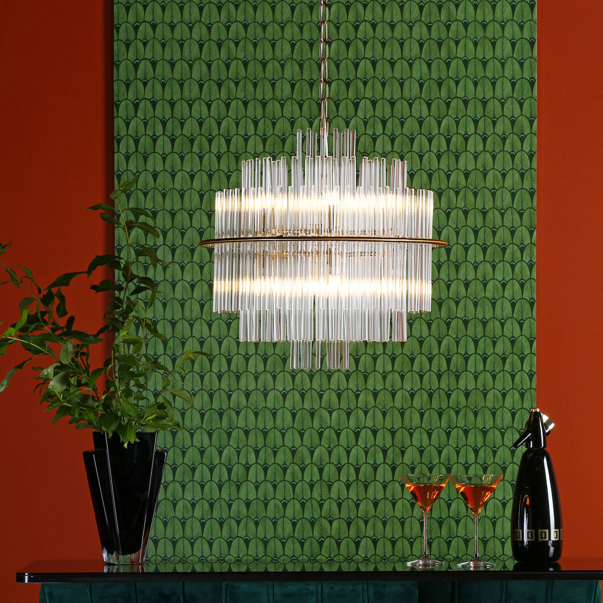A modern chandelier with glass rods hangs over a bar with drinks and a plant.