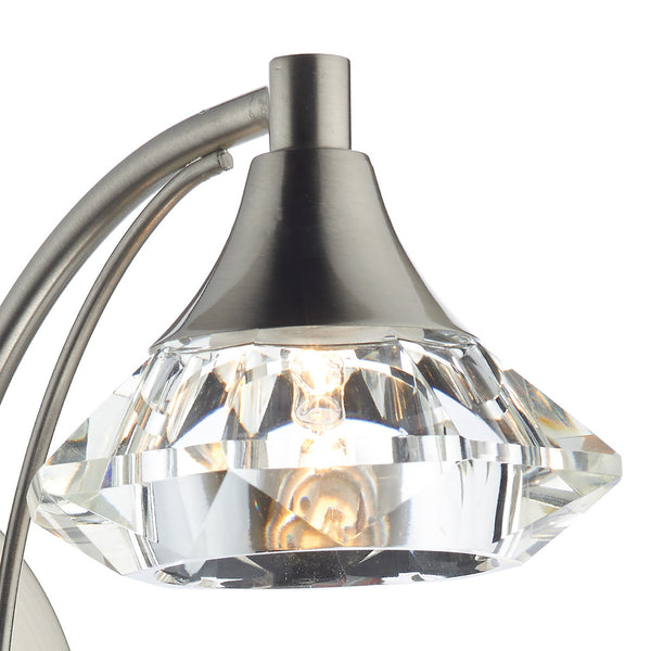 Close-up of a brushed nickel light fixture with a faceted crystal shade and glowing bulb.