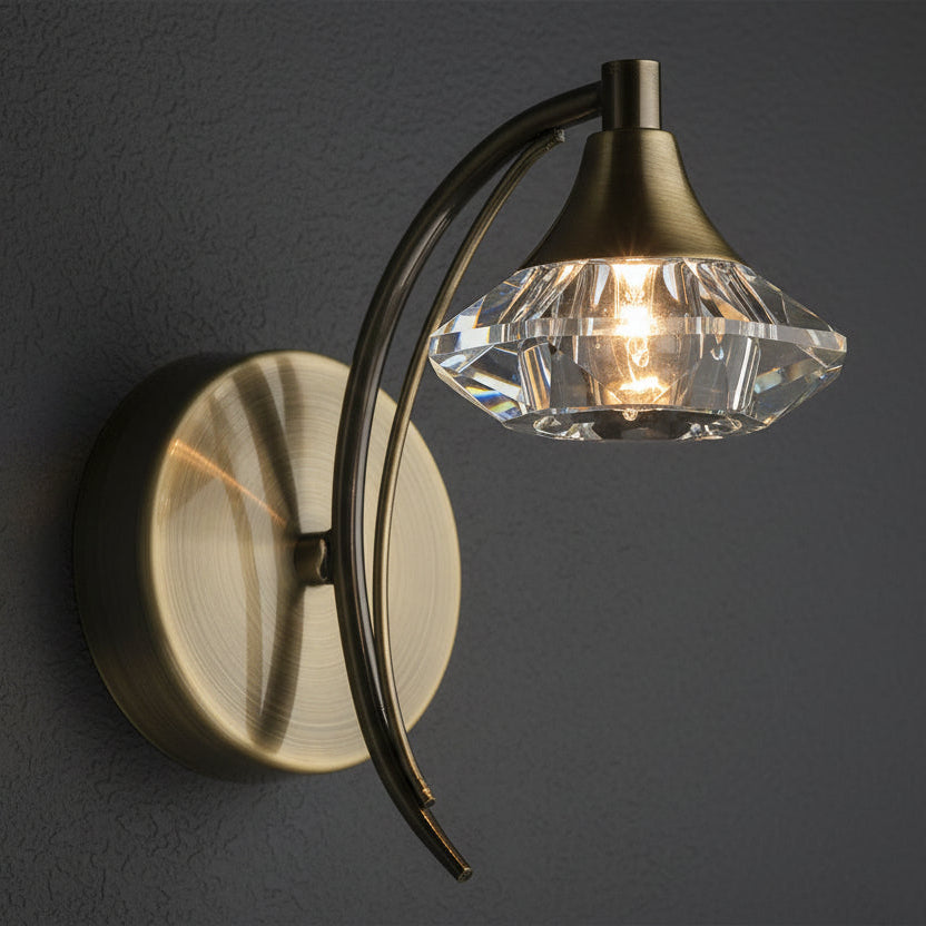Antique brass wall light with a curved arm and a faceted clear crystal shade.