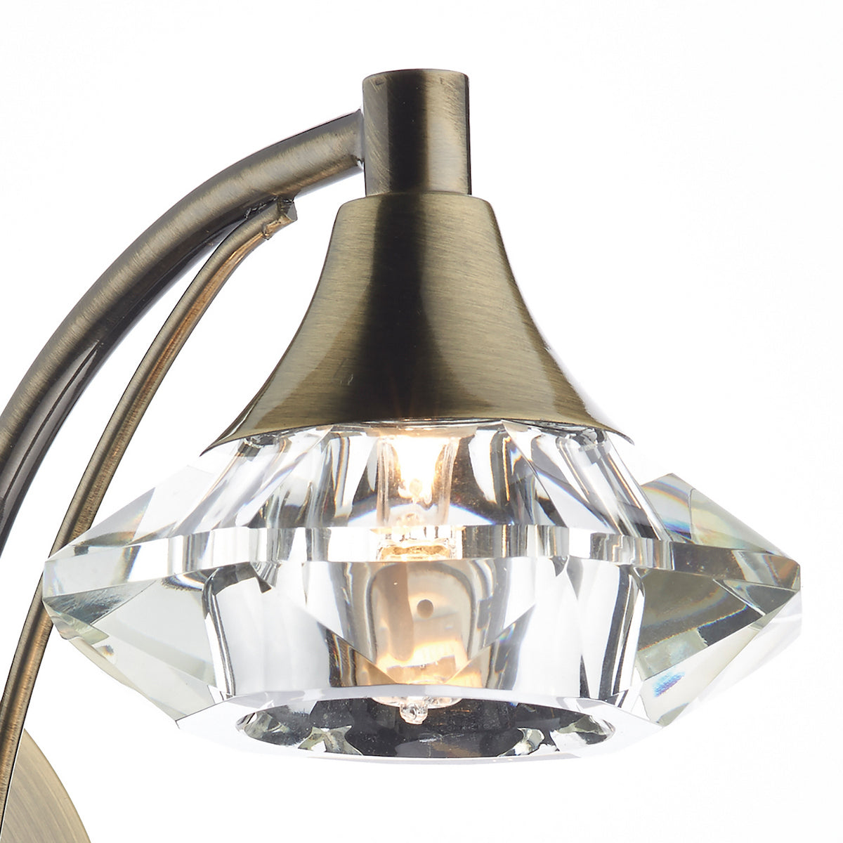 Close-up of a bronze lamp with a faceted crystal shade and a glowing bulb.