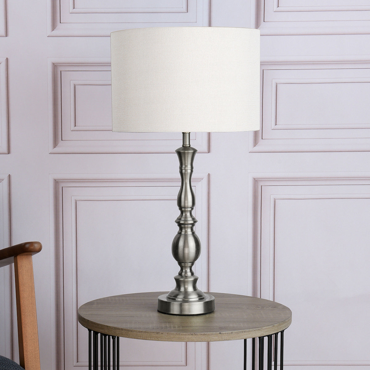 Brushed nickel table lamp with a white fabric shade on a round wooden table.