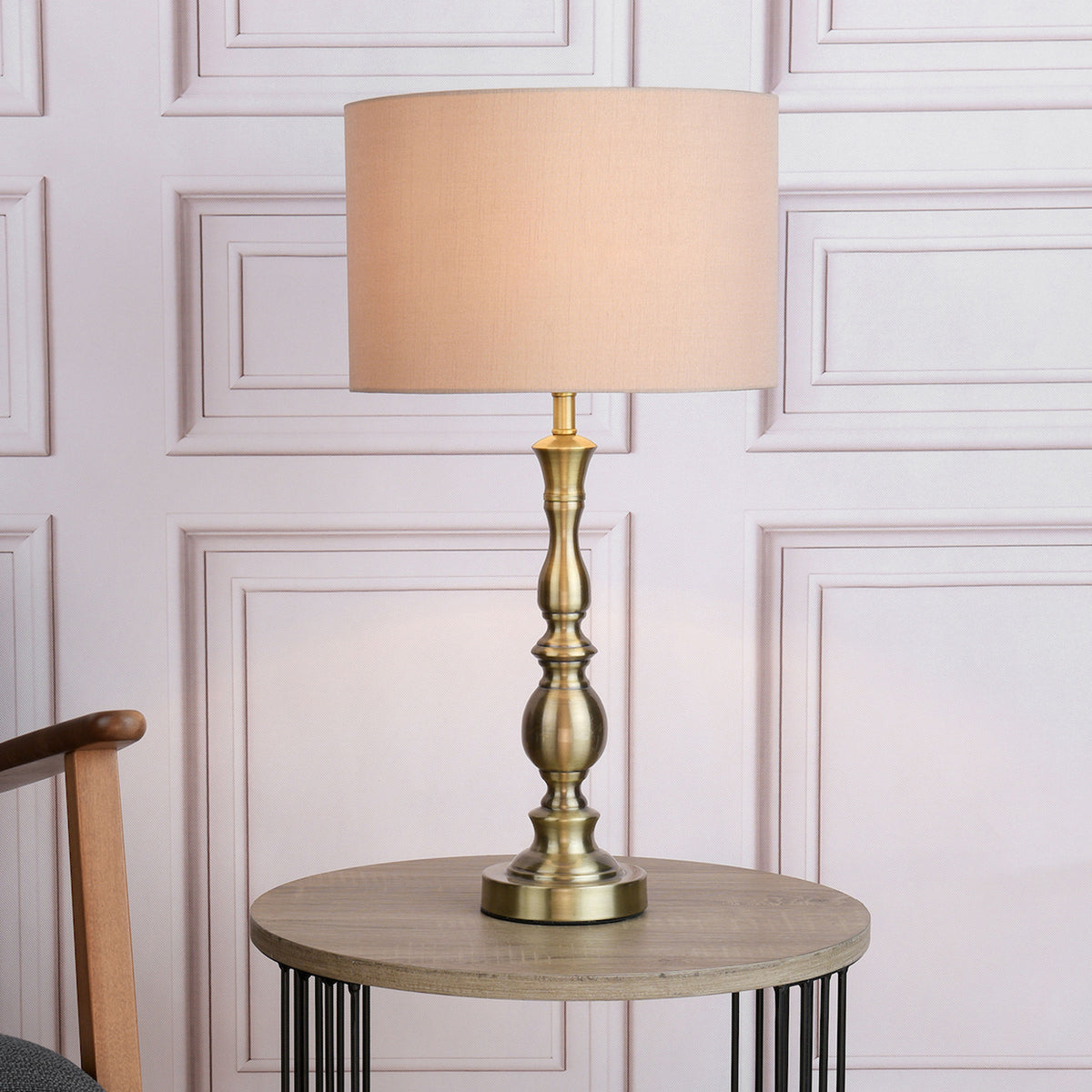 A tall, antique brass table lamp with a beige fabric shade sits on a round wooden side table.