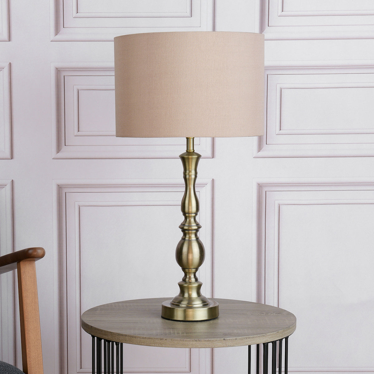 Tall antique brass table lamp with a beige fabric shade on a round wooden table.