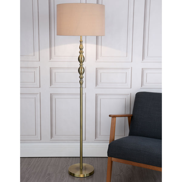 A tall, antique brass floor lamp with a beige fabric shade stands next to a dark gray armchair.