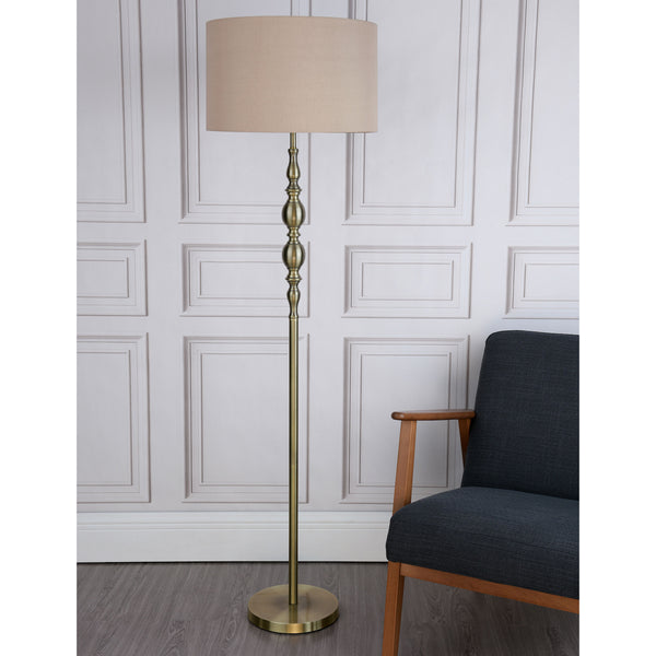 A brass floor lamp with a beige shade stands next to a dark gray armchair with wooden arms.
