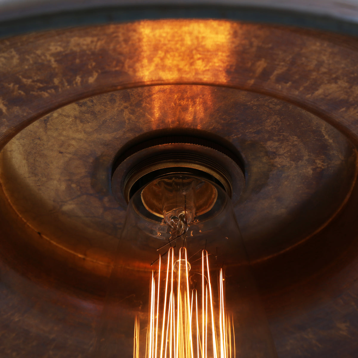 Close up of a vintage style Edison light bulb with a warm glowing filament inside a metallic copper pendant shade