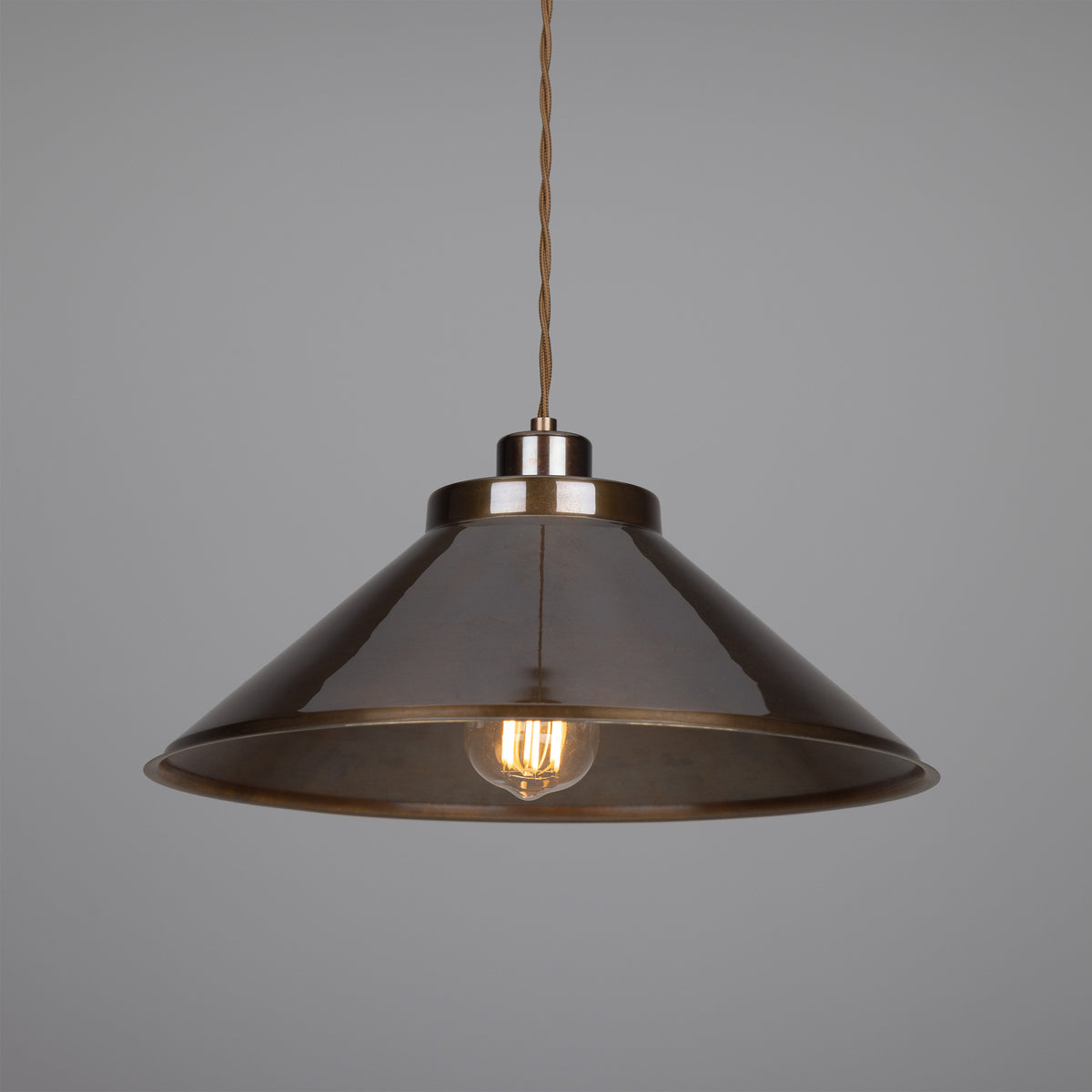 Conical bronze pendant light with an exposed filament bulb hanging from a braided cord